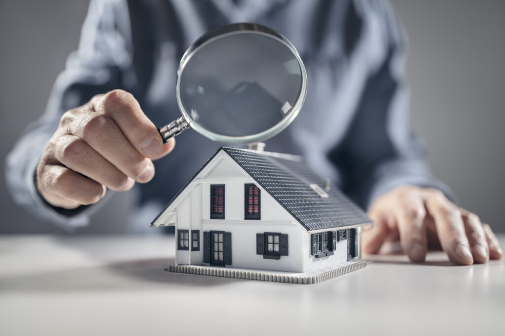 Broker reviewing a model home with a magnifying glass, the coverage review behind CANS home and auto insurance