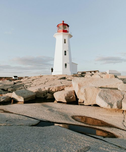 Scenic view of Peggy's Cove lighthouse with rocky foreground at sunset, Nova Scotia, Canada.