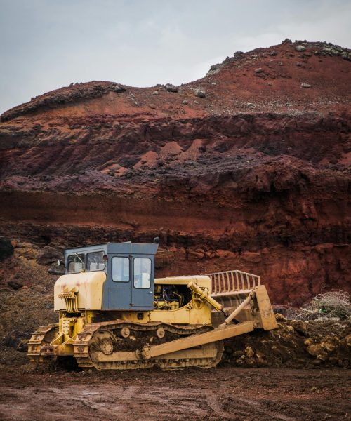 A yellow bulldozer excavating in a rugged red earth quarry under a cloudy sky.