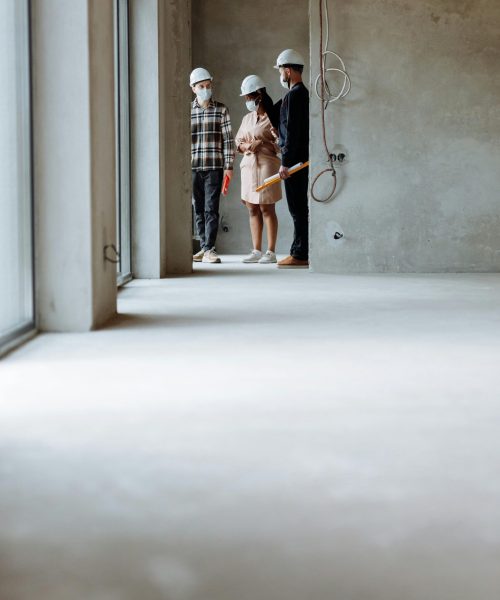 Realtors and clients wearing hard hats exploring a modern construction site indoors.
